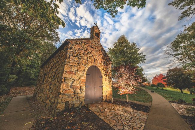 Small stone chapel with a stone path and trees around it.