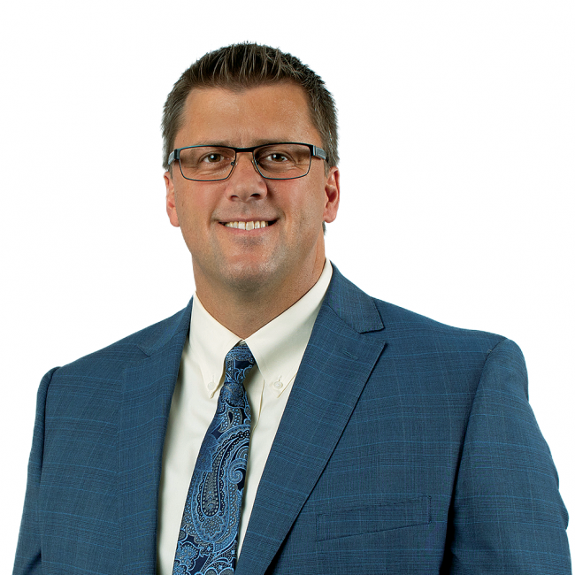 A headshot of man in a suit, tie, and glasses standing in front of a white background.