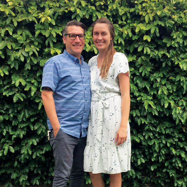 Mid-shot of man in glasses with a woman in a dress outside.