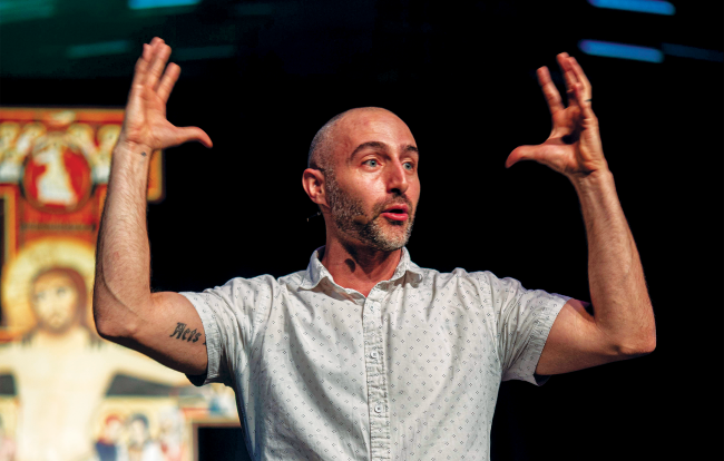 Man in a short sleeved button up shirt gestures with his hands in the air.