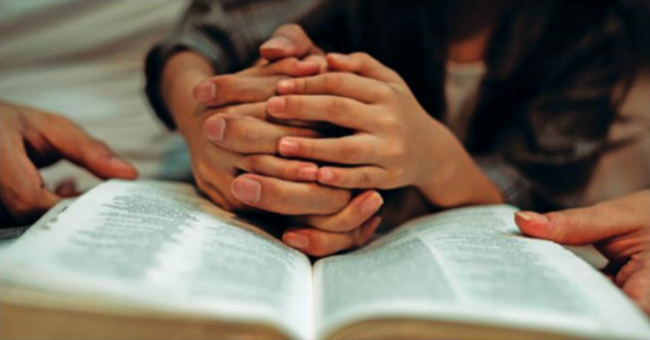 Closeup of hands holding the hands of a child with the bible open.