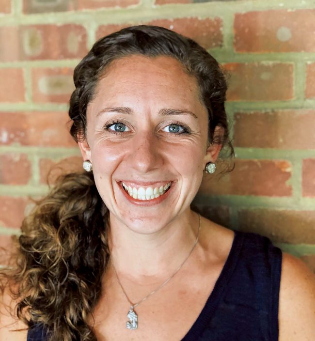Christie Fleming smiles in front of a brick wall.