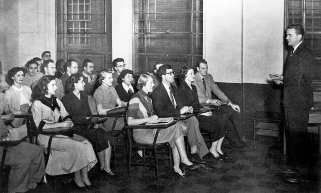 Professor speaking to classroom full of students in a black and white photo.