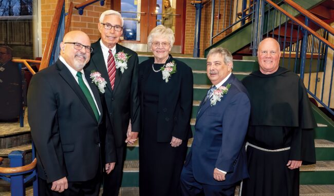 Four men and a woman in formal attire and boutonnières stand on the steps in the J.C. Williams Center.