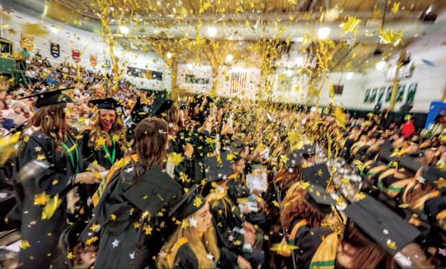 Graduates celebrate as yellow confetti stars rain down on them.