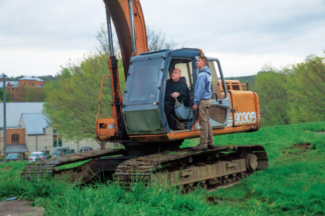 Fr. Dave Pivonka operates large backhoe under the guidance of the operator.