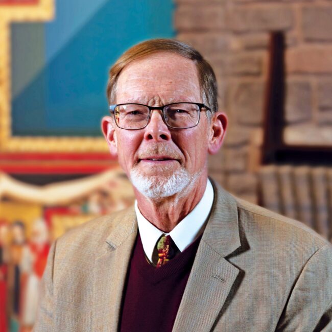 Headshot of Dr, Alan Shreck in glasses and formal attire standing in front of blurred background.
