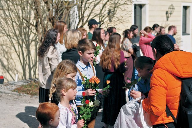 Group of children hand out roses to refugees outside.