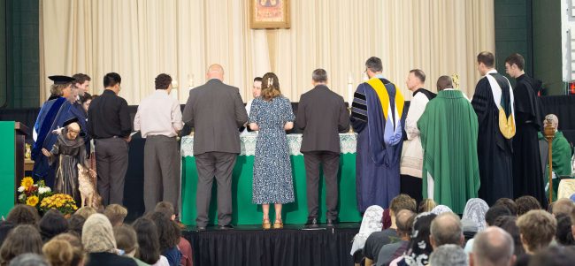 A group of people standing around an alter with their backs to the people in chairs below.
