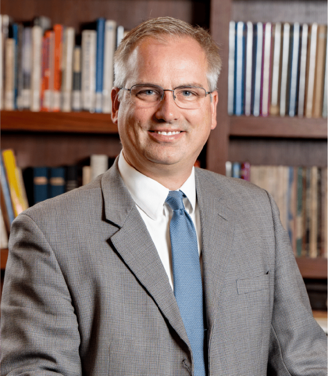 Dr. Stephen Hildebrand in a gray suit with a blurred book selves in the background.