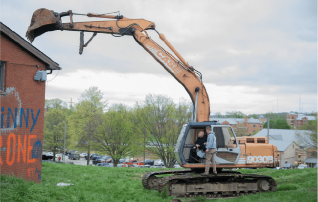 Fr. Dave Pivonka drives an excavator up to a building.
