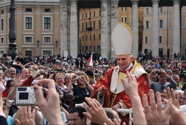 Pope Benedict XVI in a crowd with people taking pictures.
