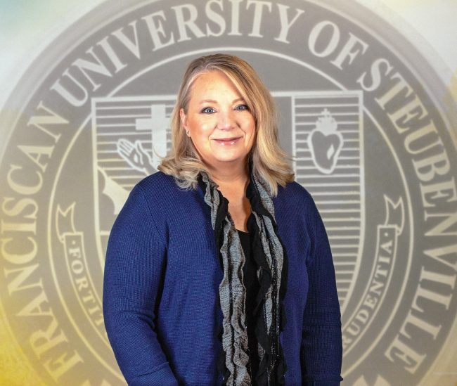 Mary Zimmerman in a blue cardigan in front of a university seal.
