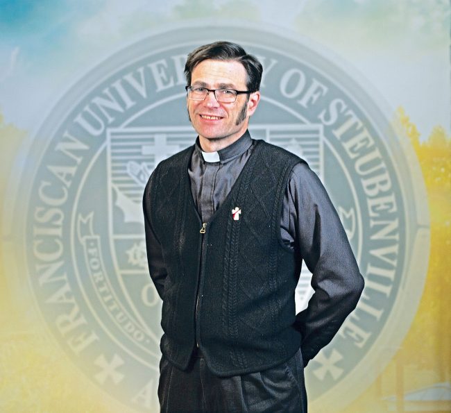 Deacon Dr. Stephan Frezza standing in front of a university seal background.