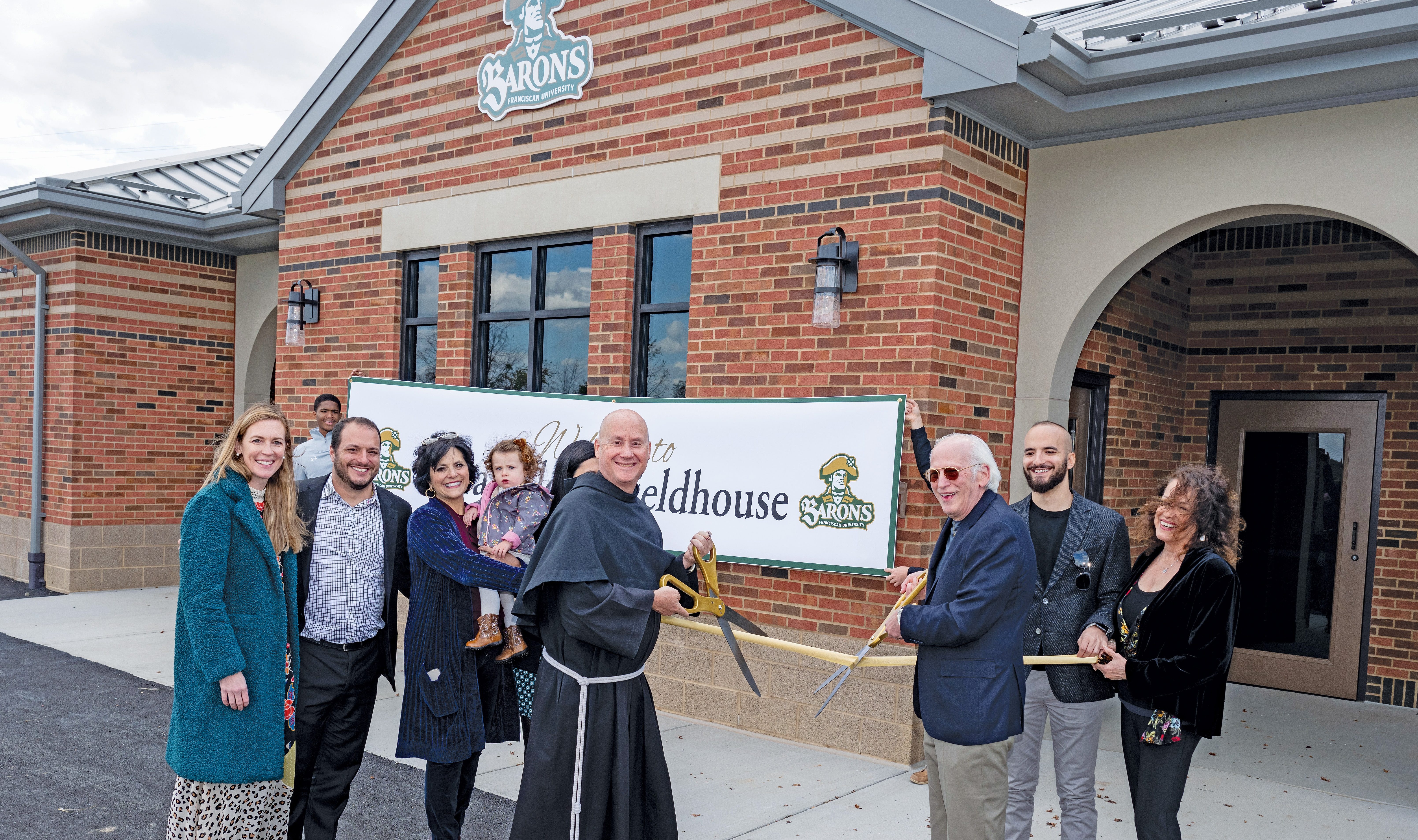 Former trustee Paul Carapellotti and Fr. Dave Pivonka, TOR, do the ribbon-cutting honors surrounded by the Carapellotti family at the new Carapellotti Fieldhouse.