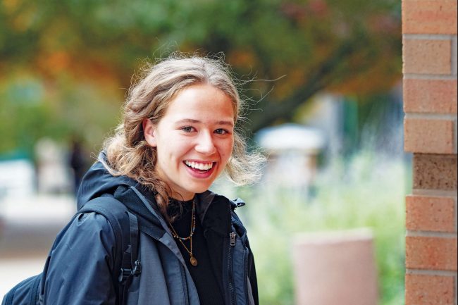 A woman smiling in a coat with a blurred nature background.