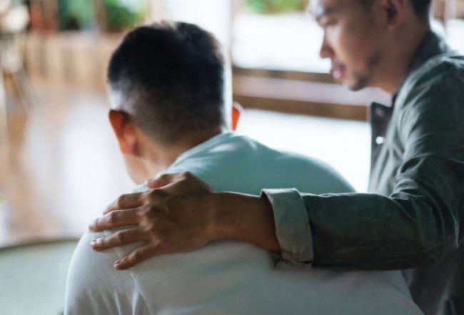 A man putting a hand on another man's shoulder in a supportive gesture.