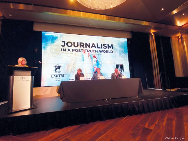 A panel of three speakers and a mediator in front of a screen that says, "Journalism in a Post-Truth World".