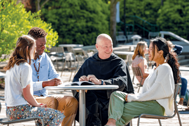 Fr. Dave Pivonka sitting with three students at outdoor seating.