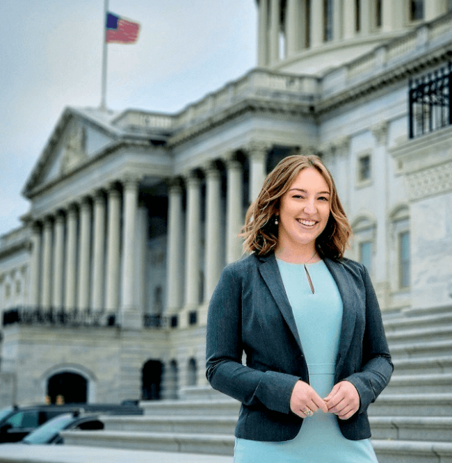 A woman in a blue dress and blazer standing in front of the Capitol Building.