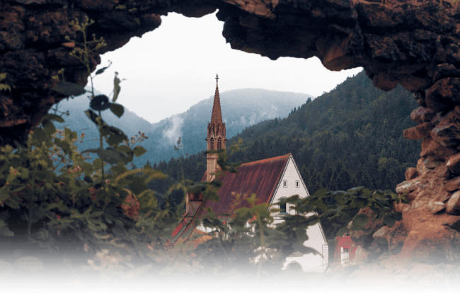A church steeple with foresty hills behind it.