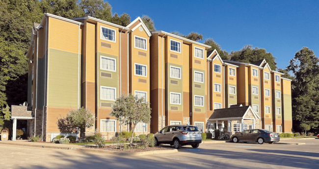 A facade of a dorm with two cars in a parking lot.
