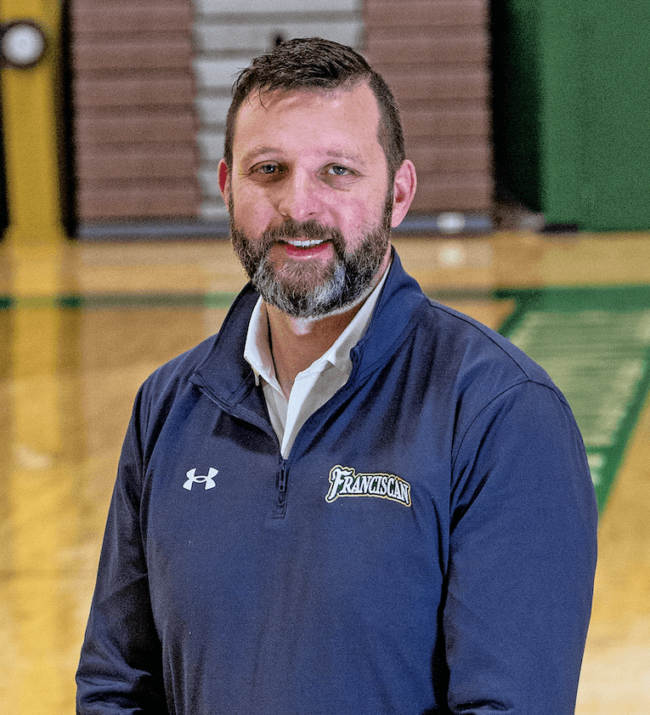 Danny Anderson in a sport shirt standing in front of a basketball court.