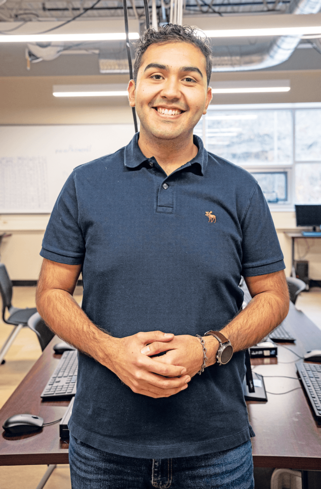 A man in a navy polo standing in a classroom.