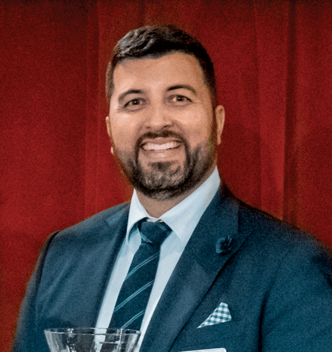 Dr. Brian Tullius in a blue suit in front of a red curtain.