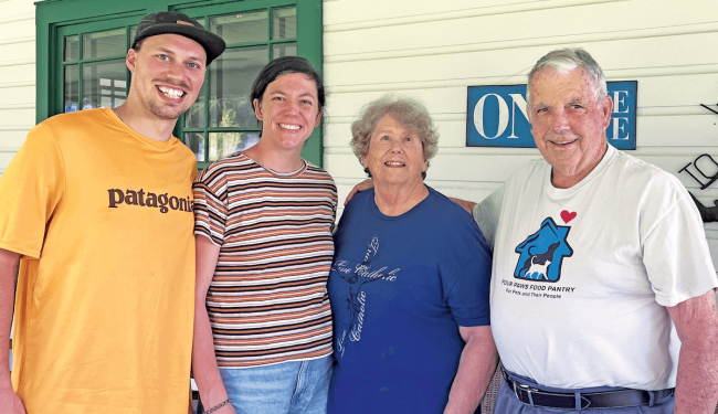 Two young people with a older couple smiling in front of a house.