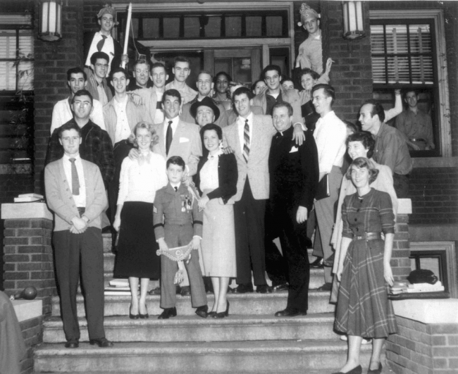 A black and white photo of a group of people standing on stair steps going up into a building.