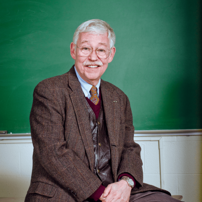 Dr. Robert C Doyle in a suit sitting in front of a chalkboard.