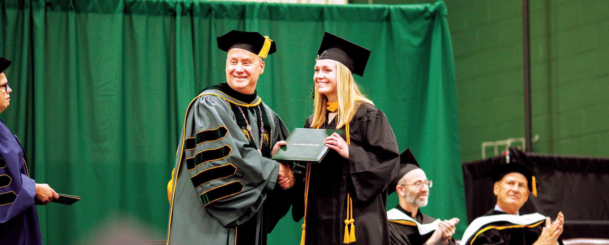 Michaela Miller receives her diploma from Fr. Dave Pivonka, TOR ’89.