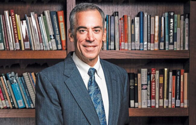 Ronald Bolster in a suit standing in front of a book shelf.