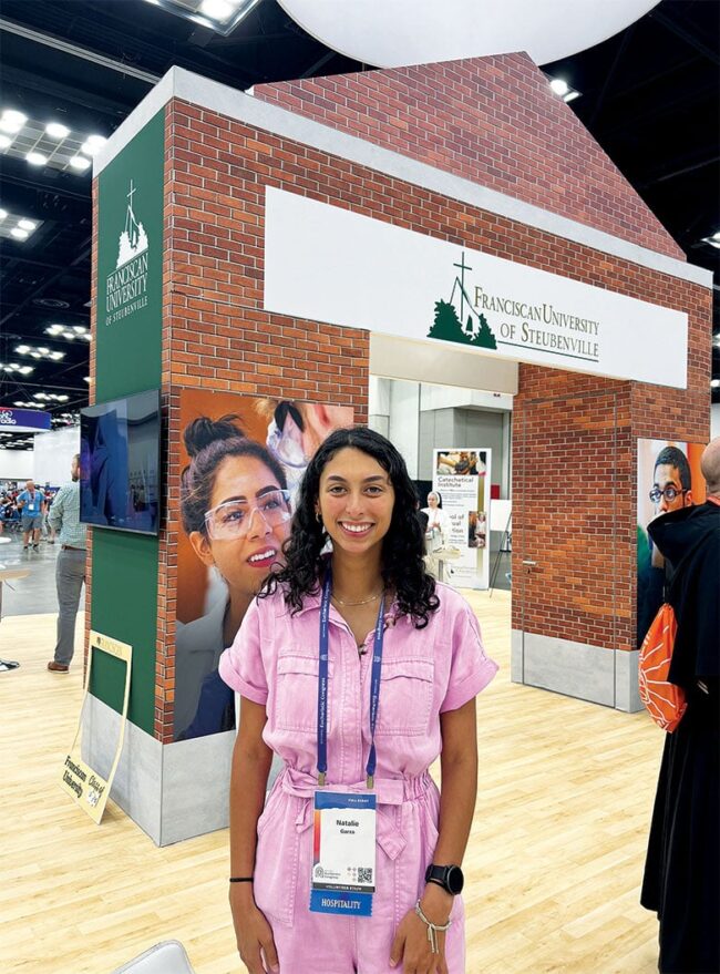 Natalie Garza in a pink jumpsuit in front of an arch in a conference room.