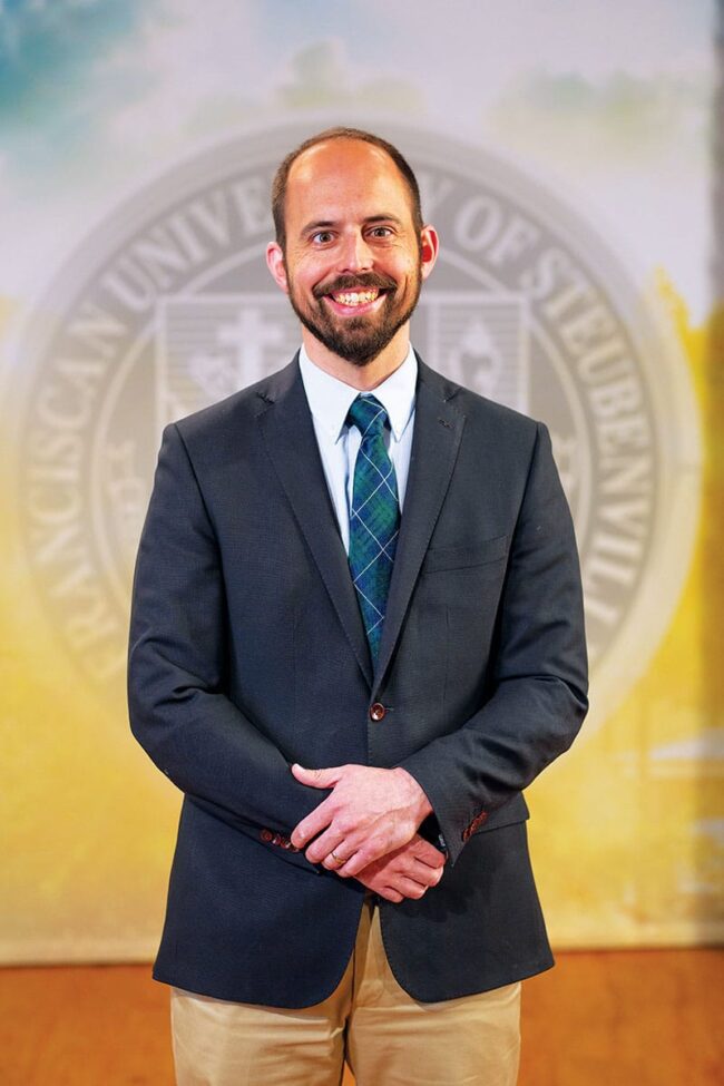 Dr. Ben Reinhard in a suit in front of a university seal background.