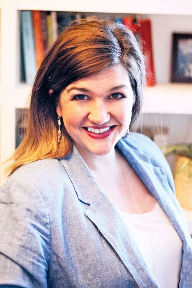 Abriana (Flynn ’06) Chilelli in a blue blazer standing in front of a blurred bookshelf.