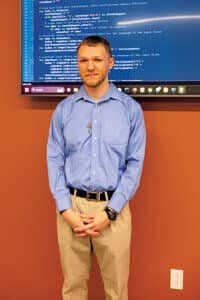 David Nalywajko standing in front of a large computer monitor.