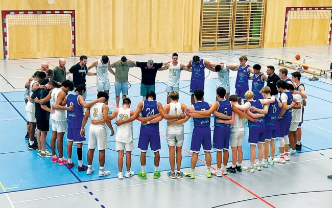 A circle of basketball players saying a prayer on a court.