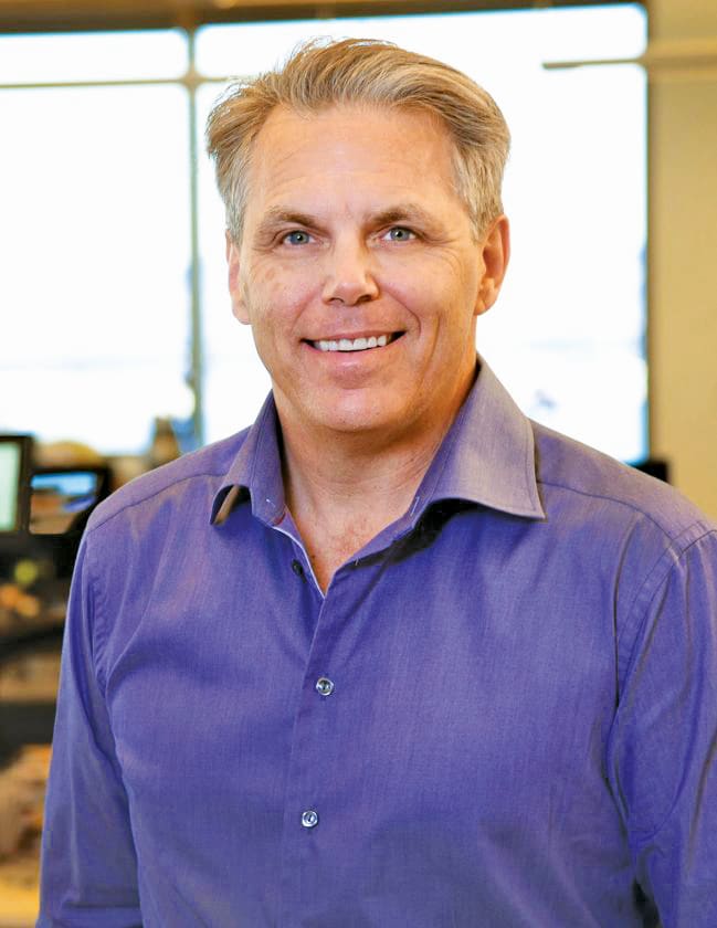 Headshot of Bob Olsen in a blue dress shirt in an office space