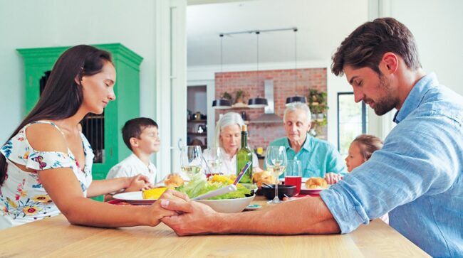 A family holding hands around a table as they pray over a meal.