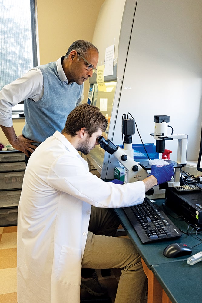 Dr. Joseph Pathakamuri and Joe Rohde looking through a microscope as they are researching cancer treatments.