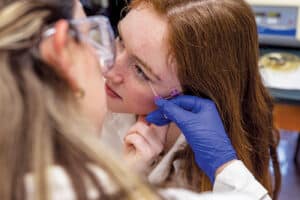 Ella Pemberton providing tears for an ELISA test as a scientist collects it with a tool.
