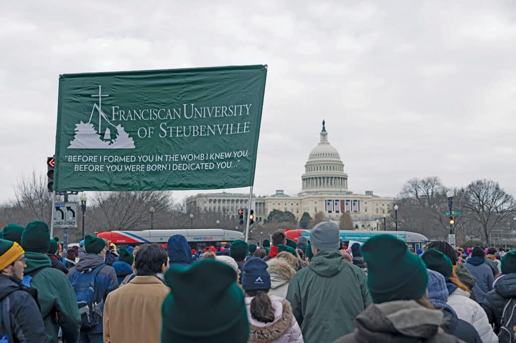 A crowd at the 2025 March for Life standing in front of the Capital Building with a large banner that has the name of the university.