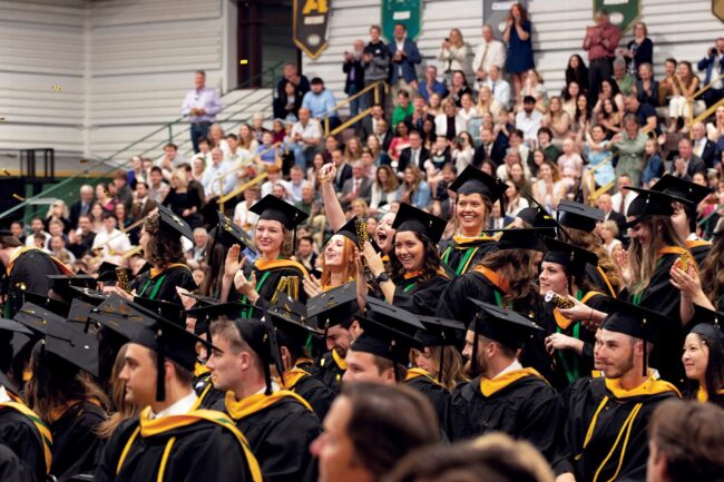 A group of university students in graduation gowns and hats, clapping.