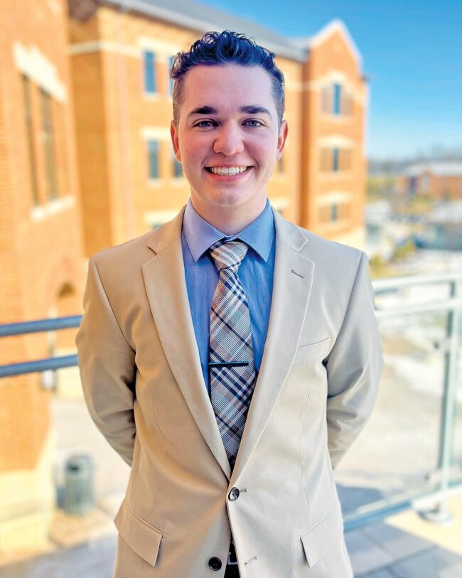 Anthony Fontecchio wearing a suit and tie with a brick building in the background.
