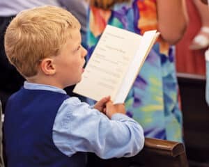 Child at solemn blessing of Christ the King Chapel holding a program.