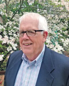 Dan Schmidt in professional wear standing in front of flowers. 