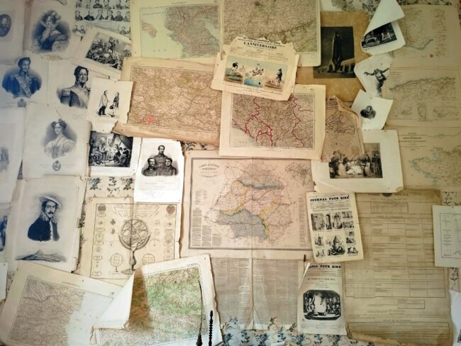 A wall covered with black and white photos of people and old maps.