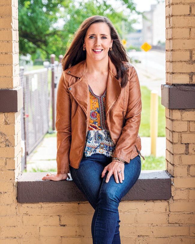 Kate Milligan sitting in an window, wearing a leather jacket and jeans.